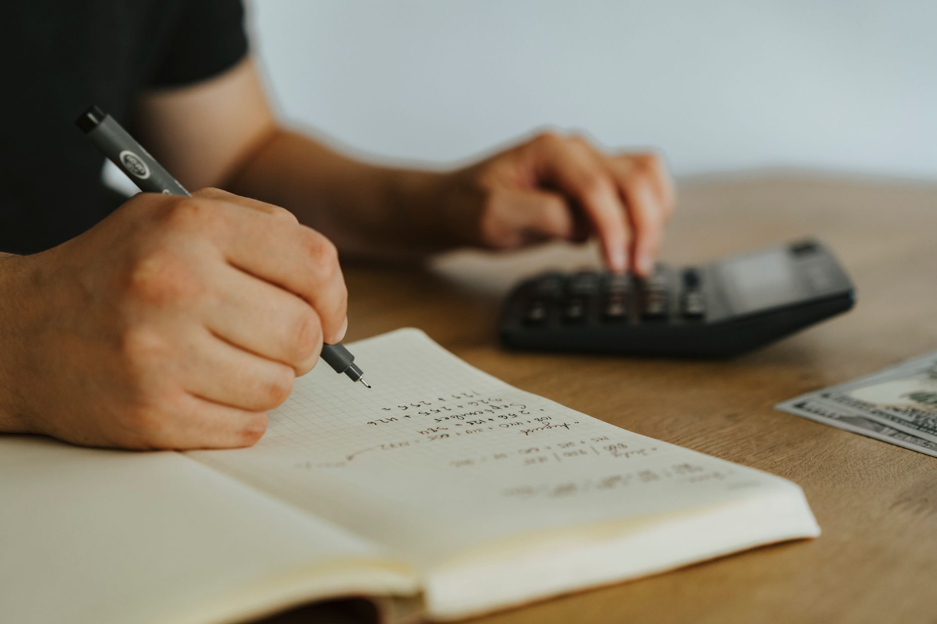 leaseradius-1786890844707 Close-up of hands writing calculations in a notebook with a calculator, focused on budgeting or financial work.