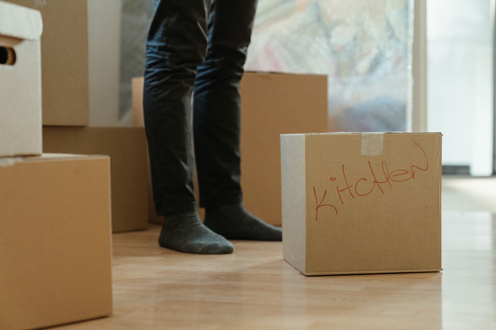 leaseradius-1790515921037 A person standing in a room surrounded by moving boxes labeled for the kitchen.