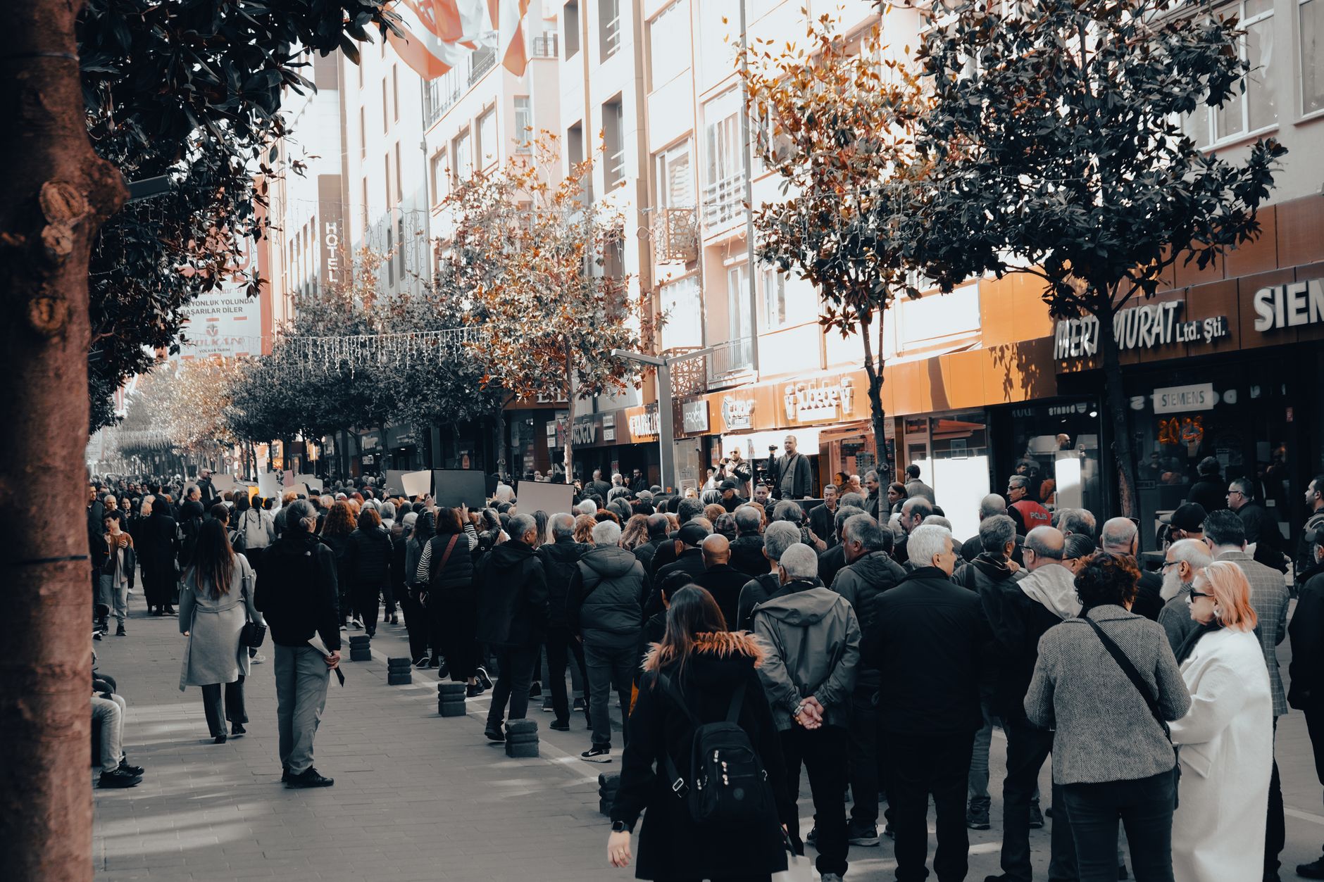 leaseradius-1790515944619 A diverse crowd walking along a city street lined with trees and shops during autumn.